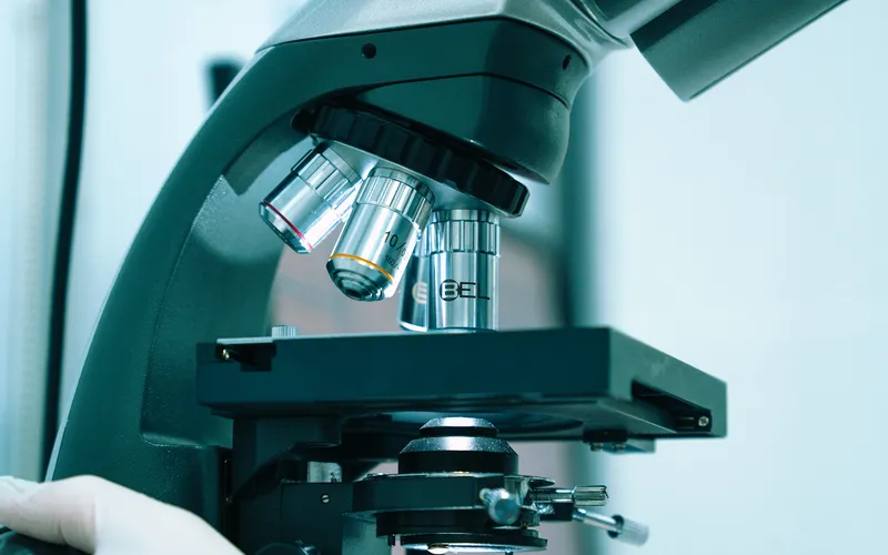 Dłoń w białej rękawiczce przy mikroskopie laboratoryjnym z kilkoma obiektywami